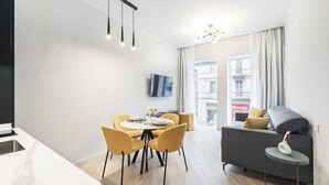 Una sala de estar moderna con un sofá, una mesa de comedor con sillas, un televisor montado en la pared y vistas al exterior a través de amplias ventanas.