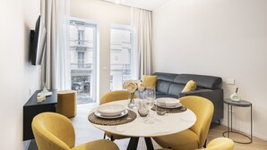 Un salón moderno con un sofá gris, sillas amarillas y una mesa de comedor para cuatro personas.