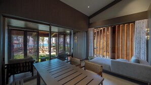 Un salon moderne avec une grande table en bois, un canapé et une vue sur l’extérieur grâce à de grandes portes-fenêtres coulissantes.