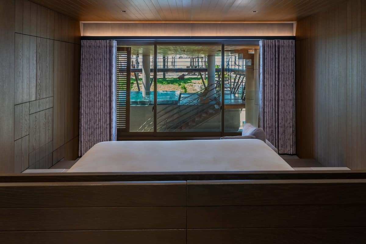 A bedroom with a large window, wooden paneling, and a view of an outdoor area with a pool and stairs.