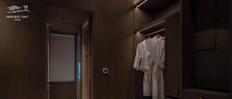 Un couloir d’hôtel moderne avec des panneaux de bois, un porte-peignoir avec des peignoirs blancs, et un aperçu d’une chambre avec un lit.