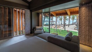 Une chambre d’hôtel moderne dotée d’un grand lit, d’un coin salon et offrant une vue sur une plage et des palmiers.