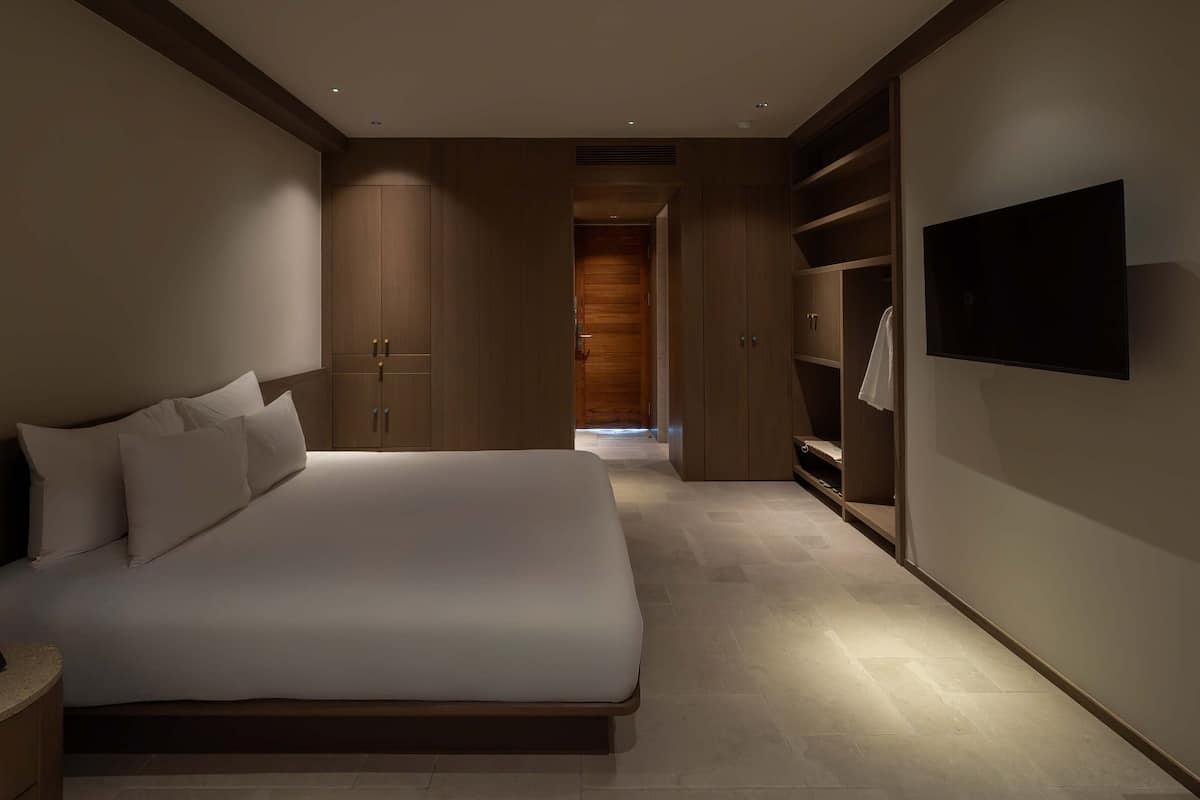 A modern hotel room with a large bed, built-in wardrobe, and a flat-screen TV.