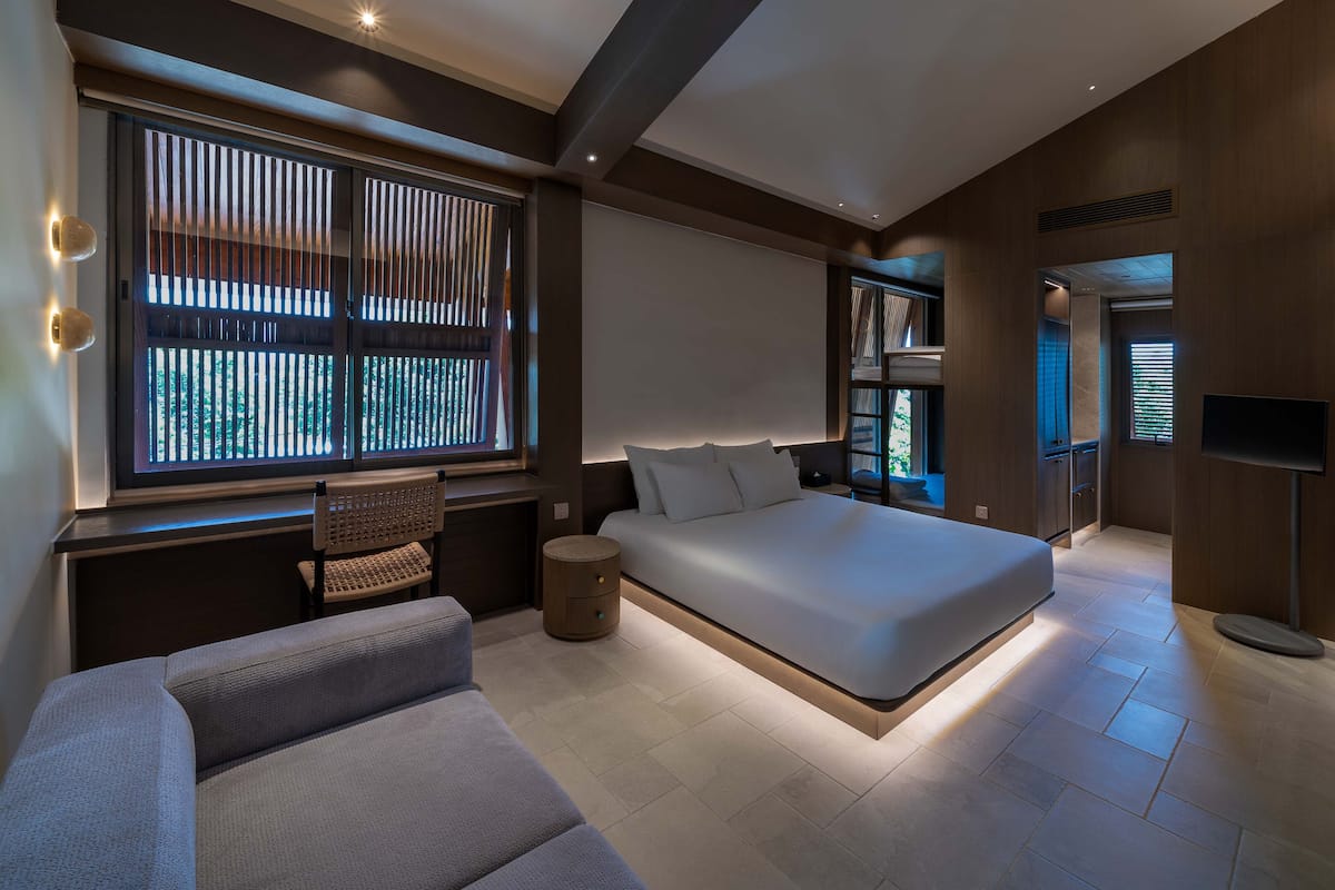 A modern bedroom with a large bed, a seating area, and a TV.