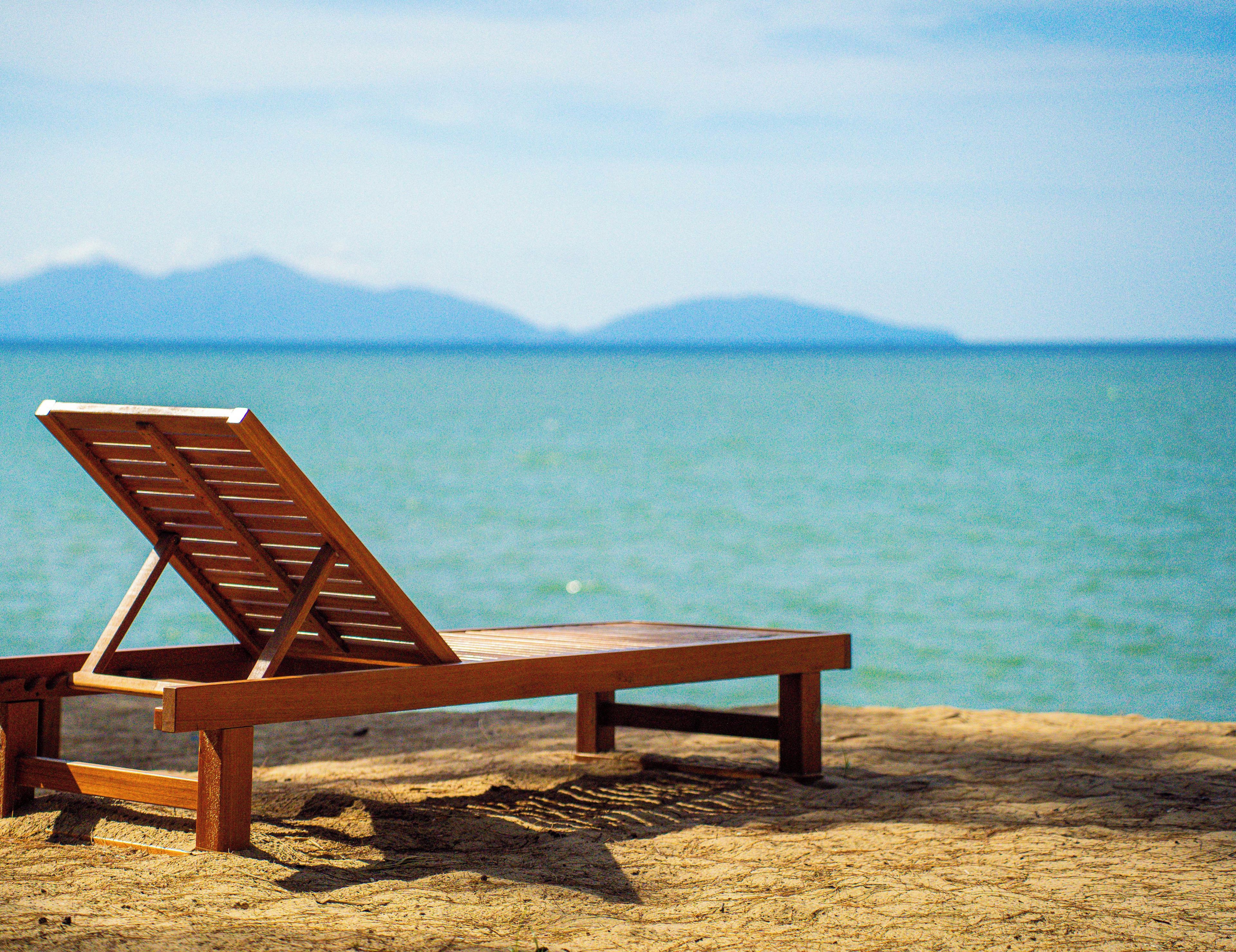Una silla de madera en la playa, con vista al mar y montañas al fondo.