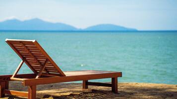 Una silla de madera en la playa, con vista al mar y montañas al fondo.