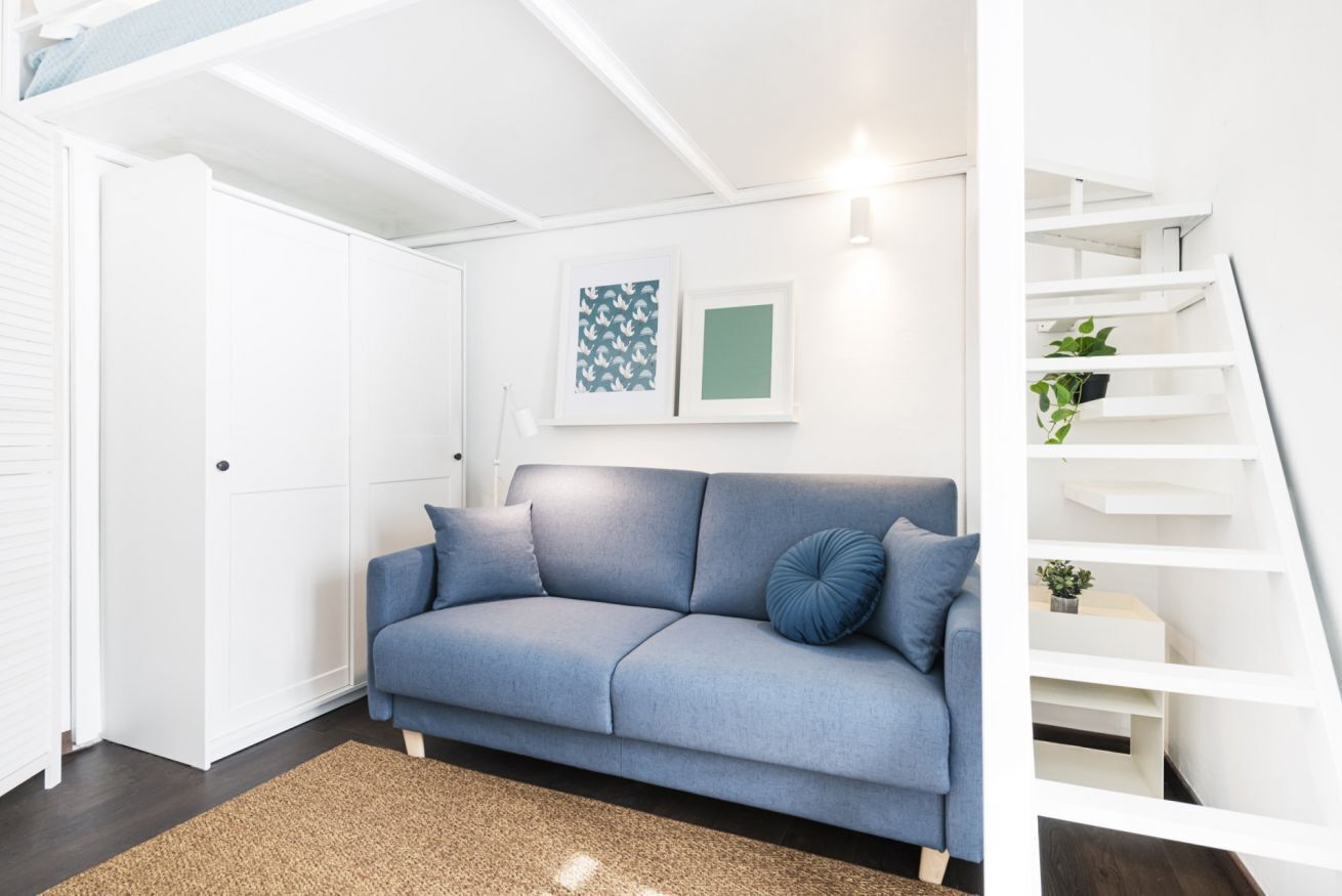 Un salon moderne avec un canapé bleu, un escalier blanc et un tableau encadré au mur.