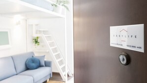 A modern living room with a light blue sofa, a white ladder, and a metal door with a contact card for EasyLife.