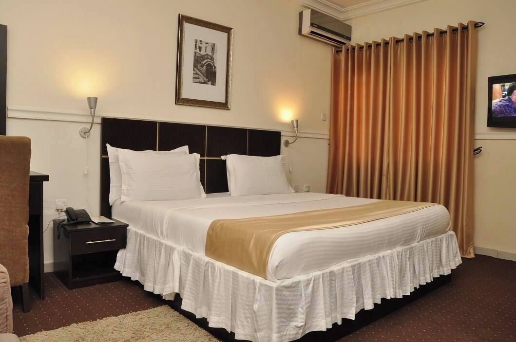 A hotel room with a large bed, two bedside tables, a nightstand, a wall-mounted TV, and a framed picture above the bed.