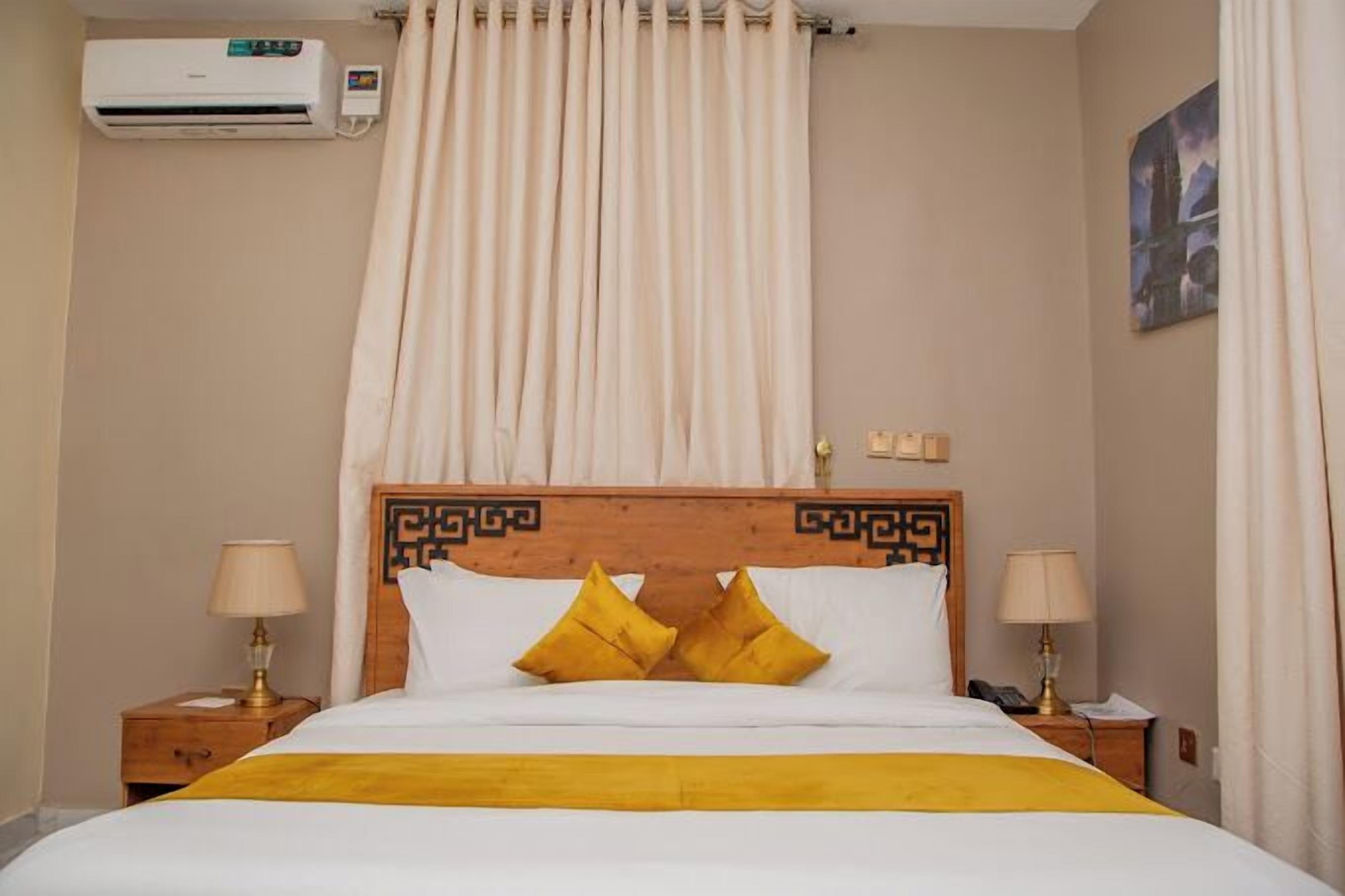 Hotelkamer met een bed, twee bedlampen, een airconditioner, een gordijn en een schilderij aan de muur.
