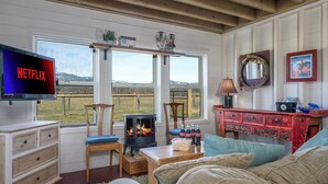 A cozy living room with a fireplace, a television displaying 'NETFLIX', and a scenic view through the windows.