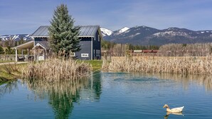 A house with a covered porch, a duck swimming in a pond, and mountains in the background.