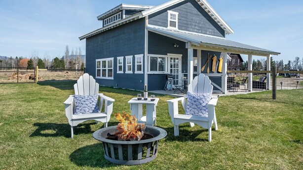 A house with a covered patio, two Adirondack chairs, a fire pit, and a dining area with outdoor furniture.