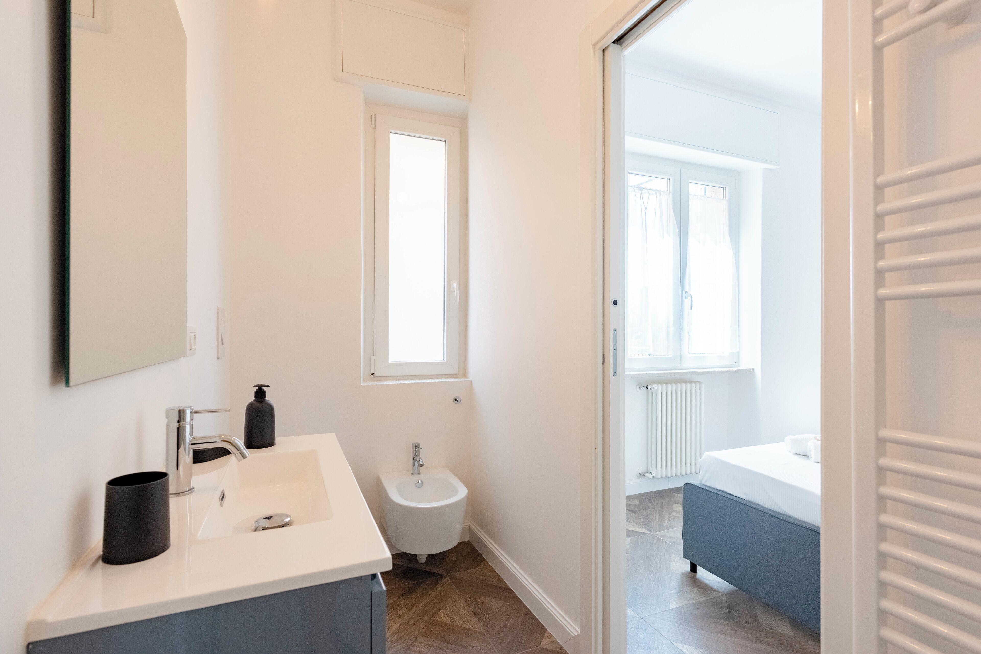 Une salle de bain moderne équipée d’un lavabo, d’un bidet et d’une baignoire, avec une fenêtre et une vue sur un balcon.