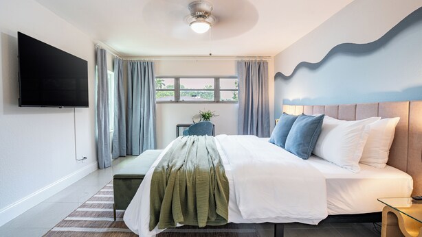 A modern bedroom with a large bed, a flat-screen TV mounted on the wall, a ceiling fan, and a window with curtains. - Your World Cup HQ: Near Miami Stadium - Pool (Fort Lauderdale)