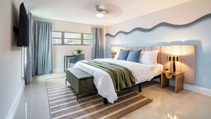 A modern bedroom with a bed, bedside tables, a bench, a TV, and a window with curtains.