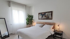 Ein modernes Schlafzimmer mit einem großen Bett, einem Holzkopfende, einem Nachttisch mit Lampe, einem Spiegel, einer Topfpflanze und einem Wandbild.