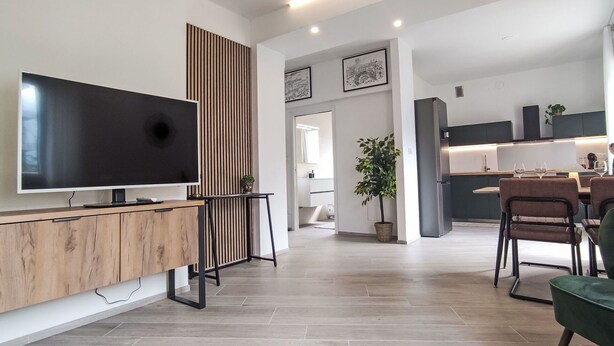 Ein modernes Wohnzimmer mit Flachbildfernseher, einer Holzkommode und einem Essbereich mit Stühlen und Tisch.