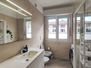 Et moderne badeværelse med en stor vask, toilet og et vindue med udsigt til bygninger.