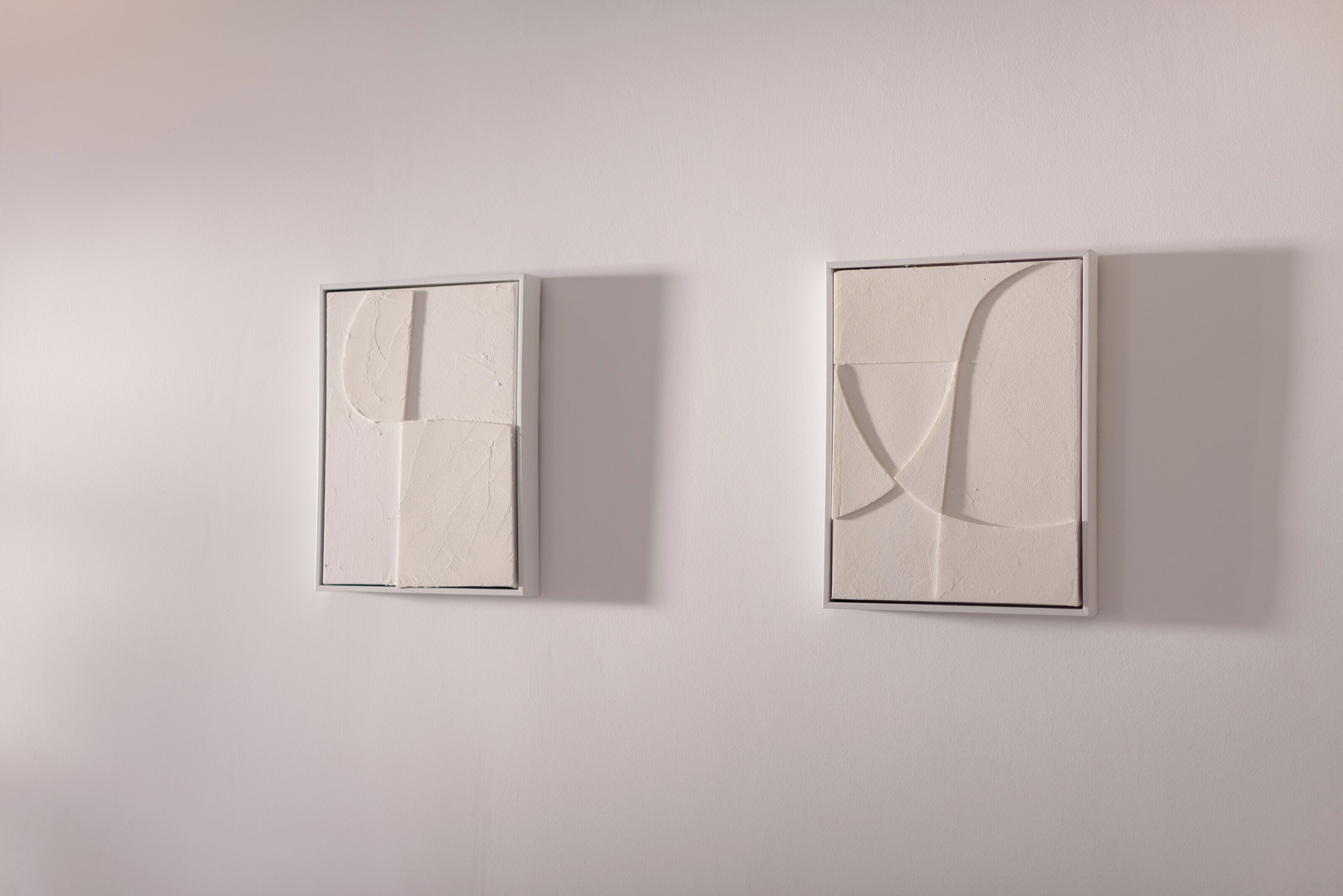 Zwei an der Wand befestigte, abstrakte Kunstwerke mit minimalistischem Design, die geometrische Formen und Linien zeigen.