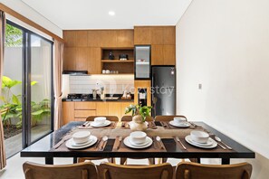 A modern kitchen with wooden cabinets, a refrigerator, and a dining table set for four with plates, cutlery, and a vase.