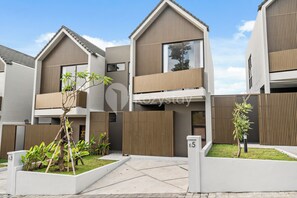 A modern residential building with a two-story design, featuring balconies and a gated entrance.