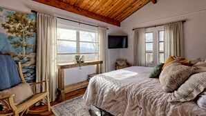 A cozy bedroom with a wooden ceiling, a large bed with patterned pillows, a rocking chair, and a painting of a landscape. - Chaco`s Chalet Cabin in the Smokies (Franklin)