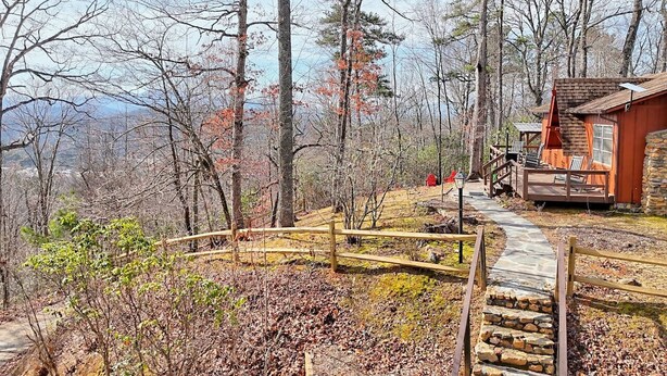 A cabin with a stone staircase leading to a wooden deck, surrounded by trees and a clear sky. - Chaco`s Chalet Cabin in the Smokies (Franklin)