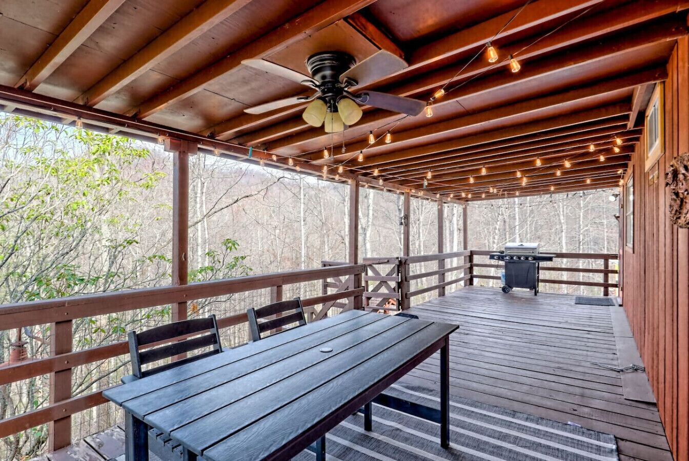Eine Terrass mit Holztisch und -stühlen, einem Deckenventilator und einem Grill.