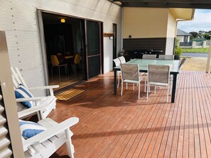 Un espacio al aire libre cubierto con una mesa y sillas, un ventanal corredero que da a un espacio interior y una terraza de madera.