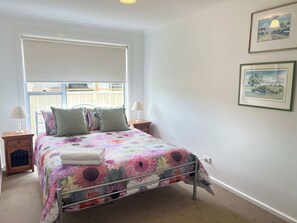 A bedroom with a bed, two bedside tables, a window, and two framed pictures on the wall.