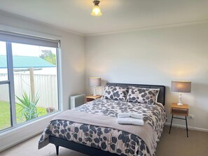 A bedroom with a bed, two bedside lamps, a window, and a view of the outside.