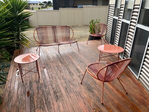 A wooden deck with metal chairs and a table, surrounded by plants and a view of a residential area.