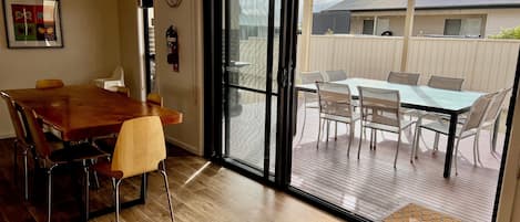A dining area with a wooden table and chairs, a sliding glass door leading to an outdoor patio with a table and chairs.