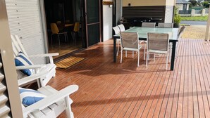 Et overdækket område med spisebord og stole, en skydedør til et indre rum og en træterrasse.