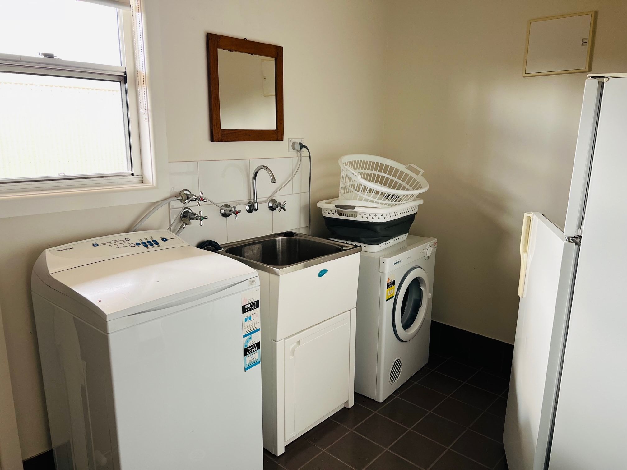 A laundry room with a front-loading washing machine, a front-loading dryer, a sink with a faucet, and a mirror on the wall.