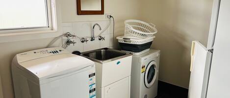 A laundry room with a front-loading washing machine, a front-loading dryer, a sink with a faucet, and a mirror on the wall.