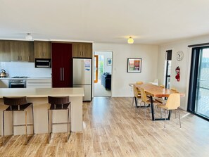 A modern kitchen with wooden cabinets, a built-in oven, and a refrigerator. There is a dining area with a wooden table and chairs.