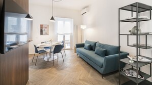 A modern living room with a blue sofa, a dining table with chairs, a black bookshelf, and a TV mounted on a wooden cabinet. - EASYLIFE – Your ideal space in Milan (Milano)