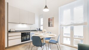A modern kitchen with white cabinets, a black oven, and a dining area with a round table and blue chairs. - EASYLIFE – Your ideal space in Milan (Milano)