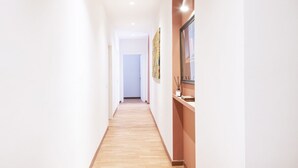 Un pasillo estrecho con suelo de madera, paredes blancas y una puerta al final.