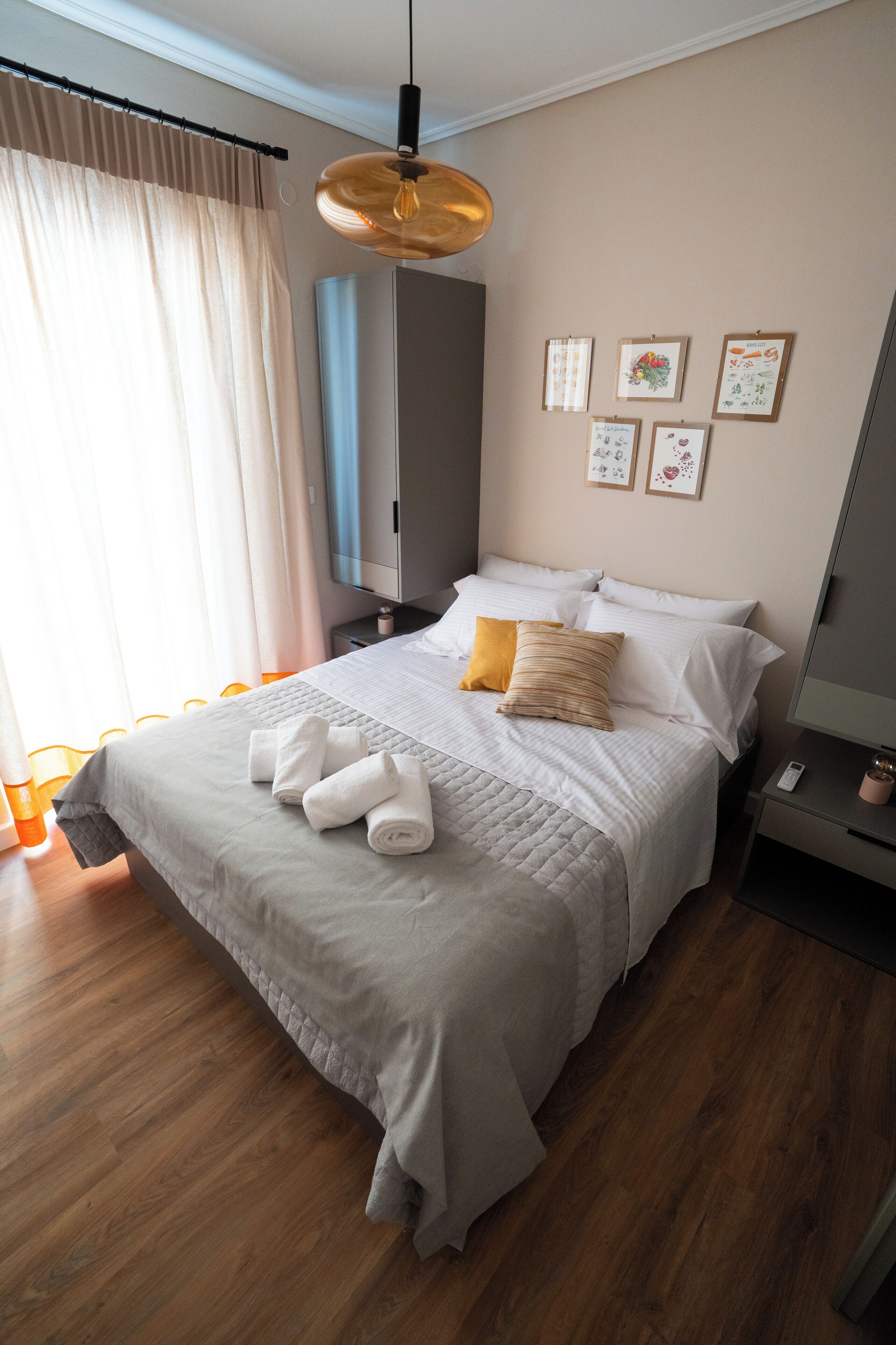 A neatly made bed with white and yellow pillows, a bedside table with a lamp, and a wall with framed pictures.