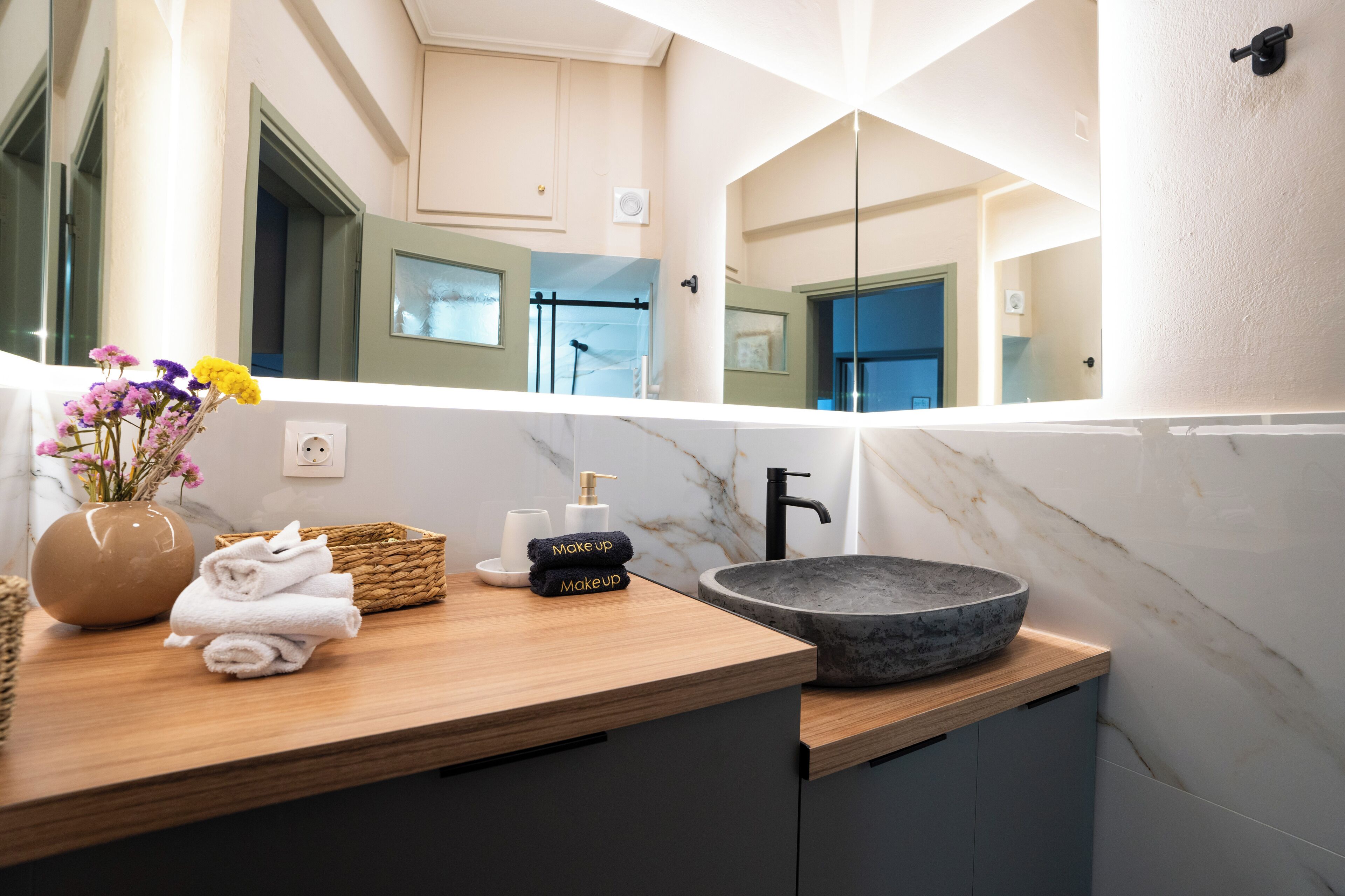 Un baño con tocador de madera, lavamanos de mármol y un espejo que refleja la habitación.