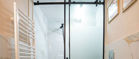 A modern bathroom with a glass-enclosed shower, a toilet, and a black trash bin.