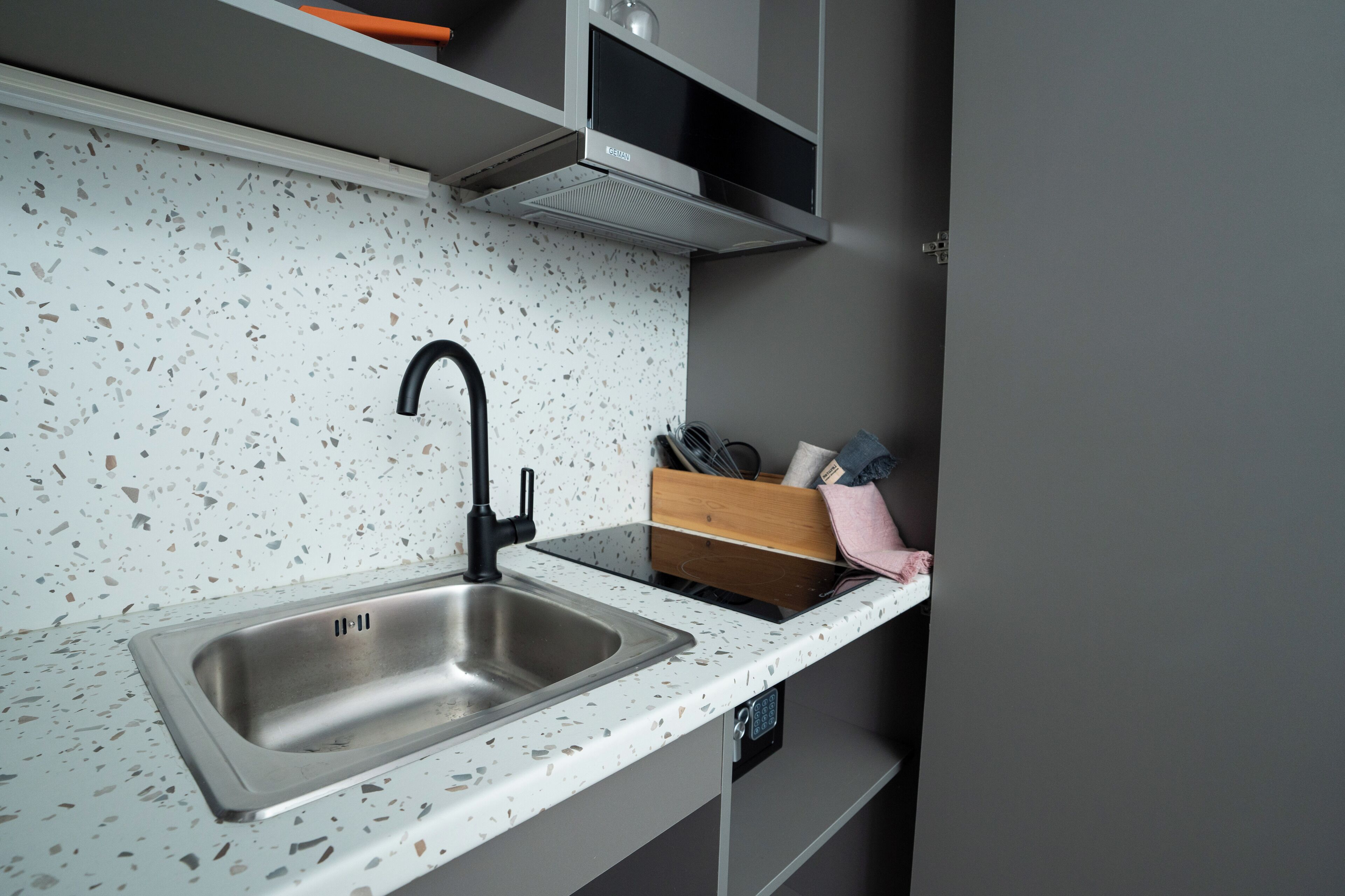 A kitchen with a stainless steel sink, a modern faucet, and a speckled backsplash.