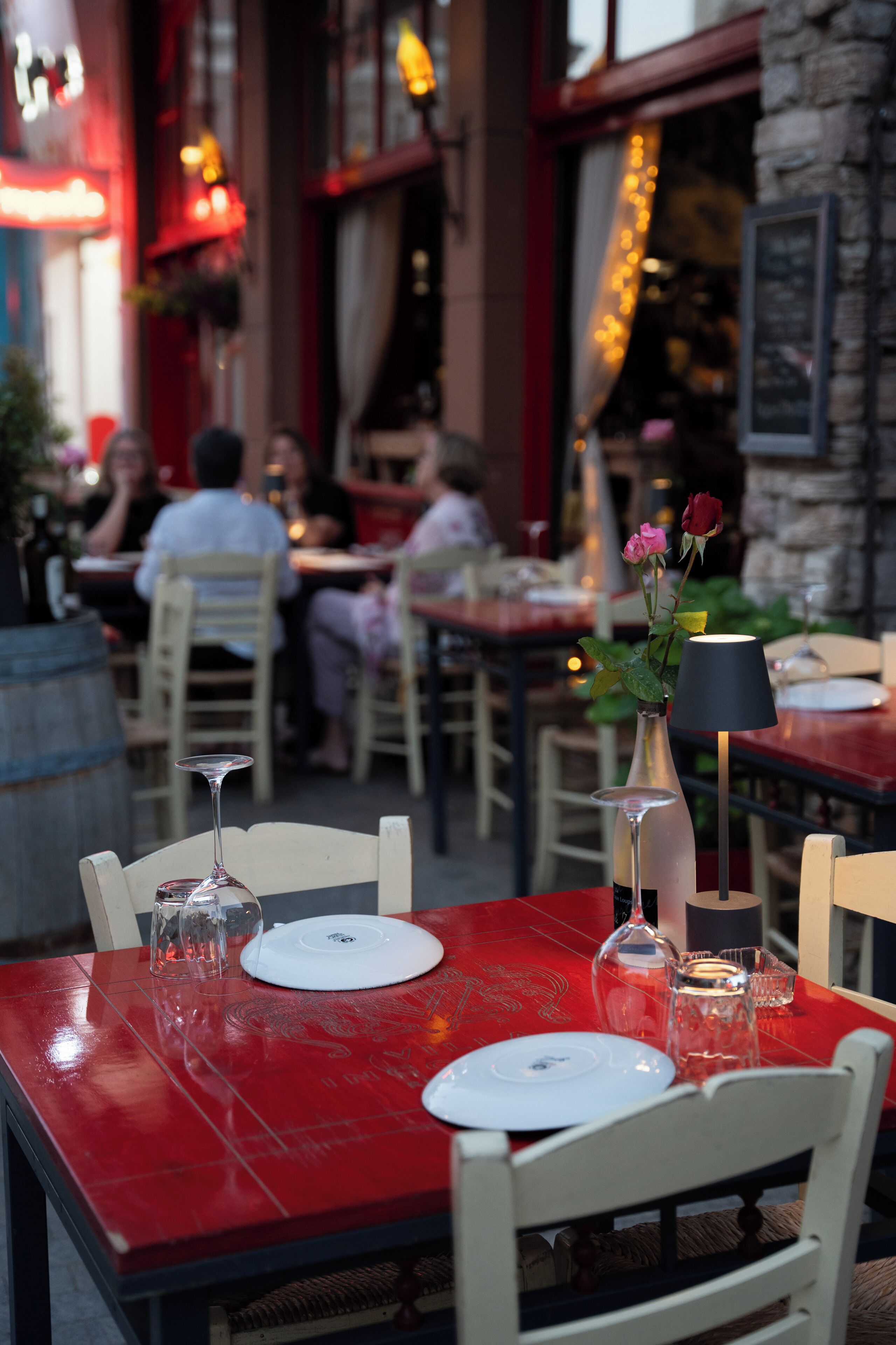 A restaurant setting with tables set for dining, a vase with flowers, and a candle on the table.