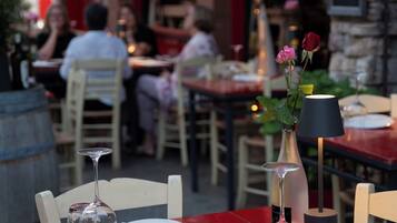 A restaurant setting with tables set for dining, a vase with flowers, and a candle on the table.