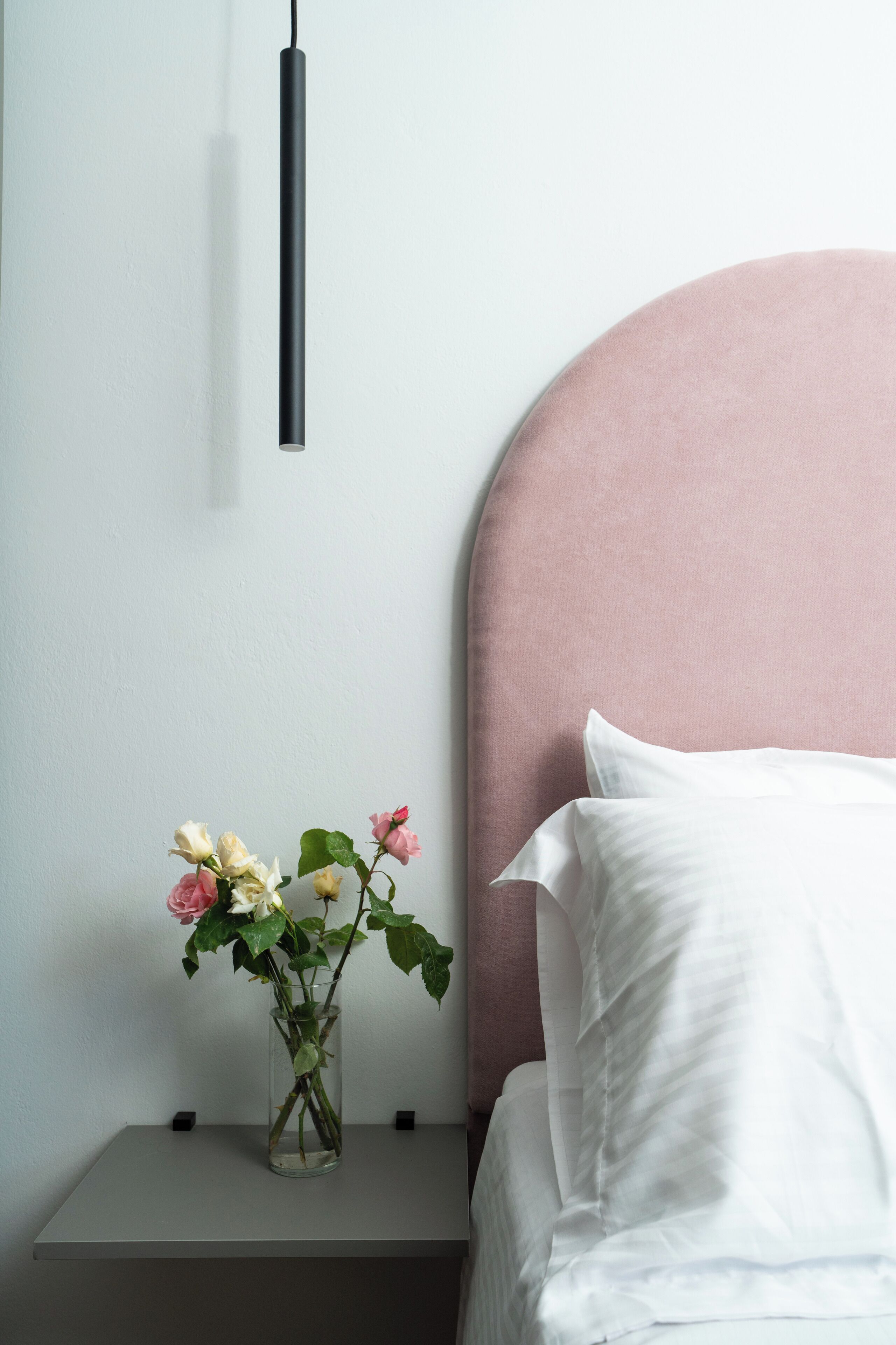 A bed with a pink headboard, a white pillow, and a vase with flowers on a bedside table.
