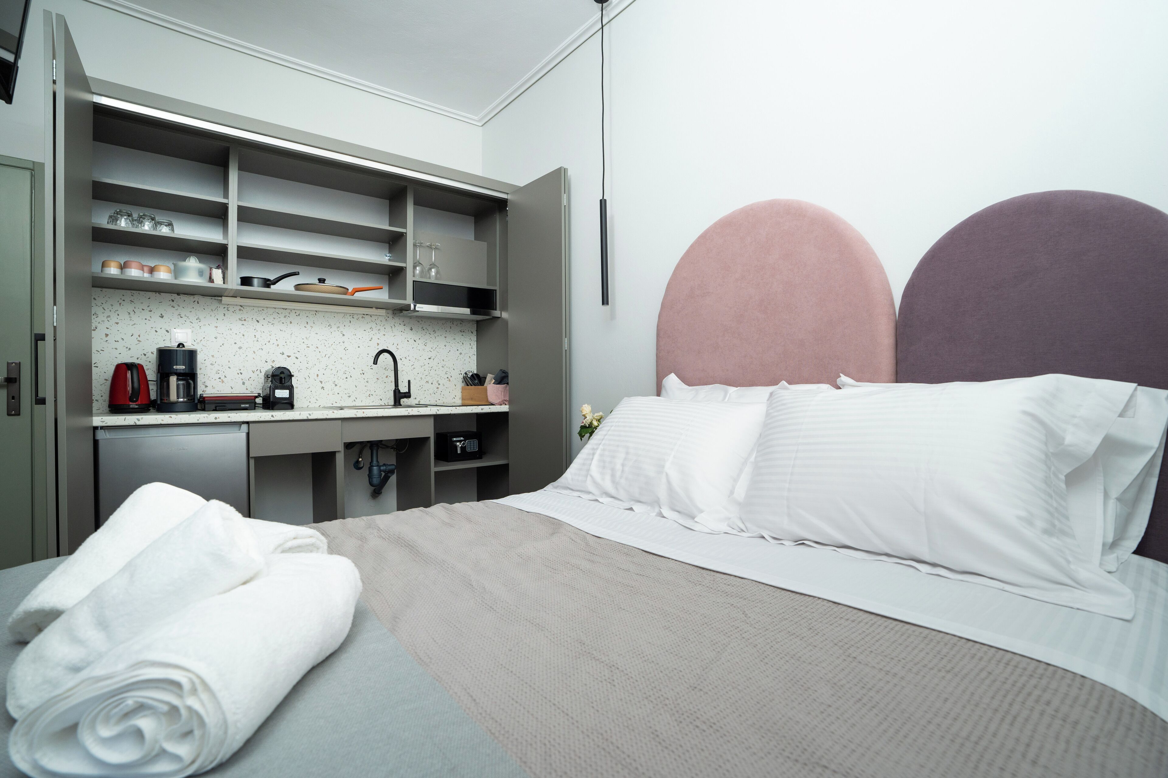 A hotel room with a bed, a desk with a coffee maker, and a built-in wardrobe.