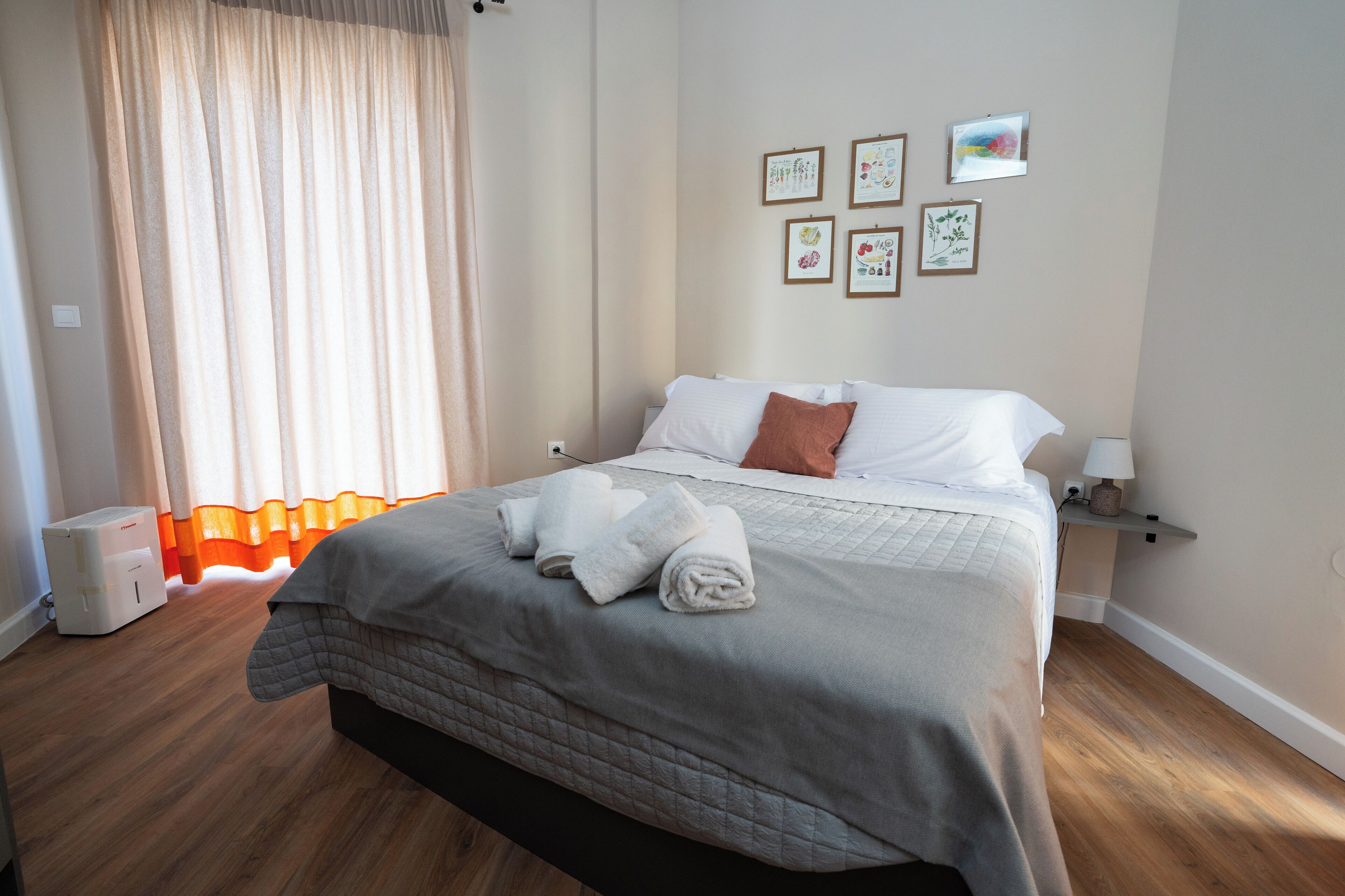 Een net opgemaakt bed met wit en bruin beddengoed, een nachtkastje met een lamp, en een muur met ingelijste foto's.